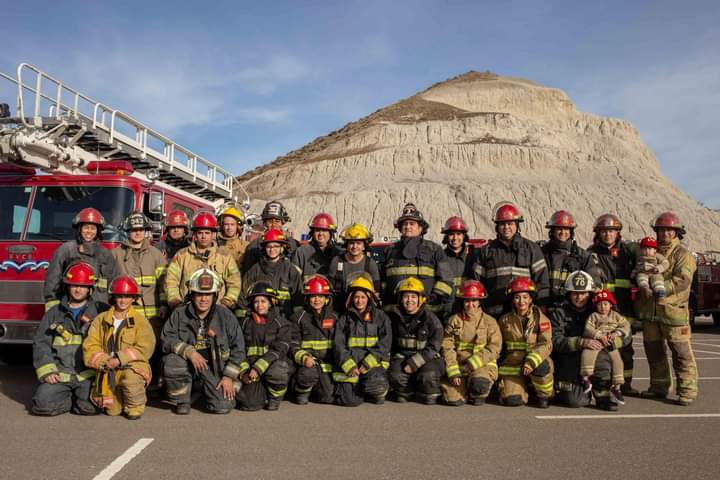 Bomberos y bomberas posando con el cerro de Comodoro Rivadavia detrás